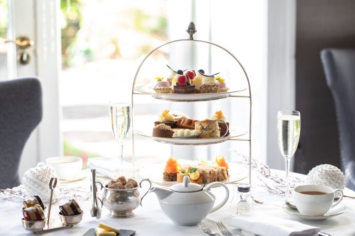 Afternoon tea set with tiered pastries, sandwiches, and champagne on a white tablecloth.