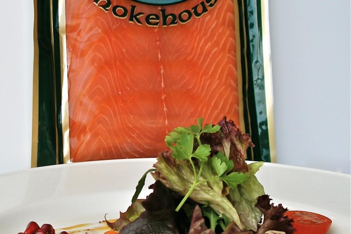 Plate with smoked salmon, mixed greens, cherry tomatoes, and pomegranate seeds, package in background.