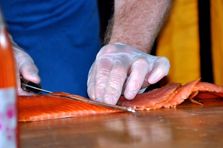 Person cutting smoked salmon with gloves on a wooden surface.