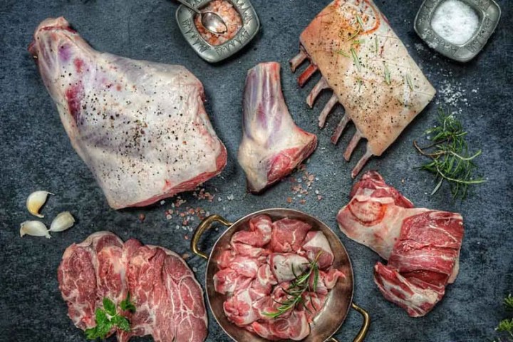 Various cuts of raw lamb meat with herbs and spices on a dark slate background.