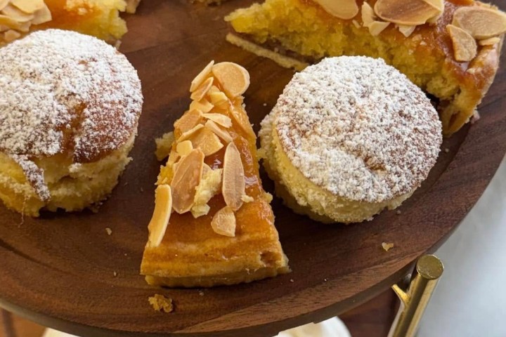 Assorted pastries with almonds and powdered sugar on a two-tier wooden stand.