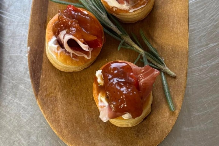Four appetizers with ham and chutney on wooden platter, garnished with rosemary.