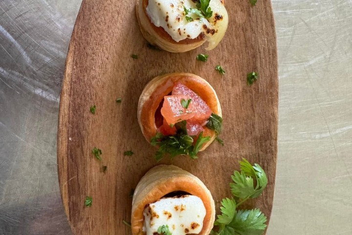 Three small gourmet appetizers on a wooden plate, garnished with herbs.