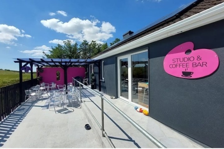 Outdoor seating area of a studio and coffee bar with pink sign and metal chairs.