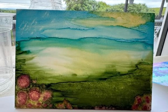 Abstract painting with green, blue, and pink hues on a table.