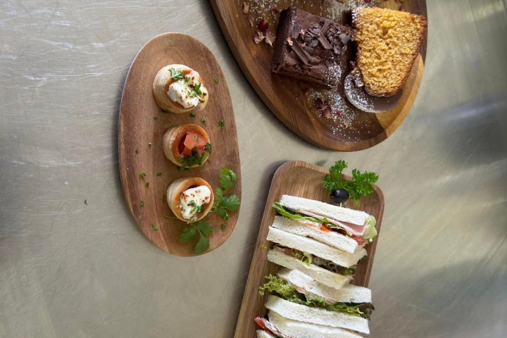 Assorted sandwiches and desserts on wooden platters on a metallic surface.