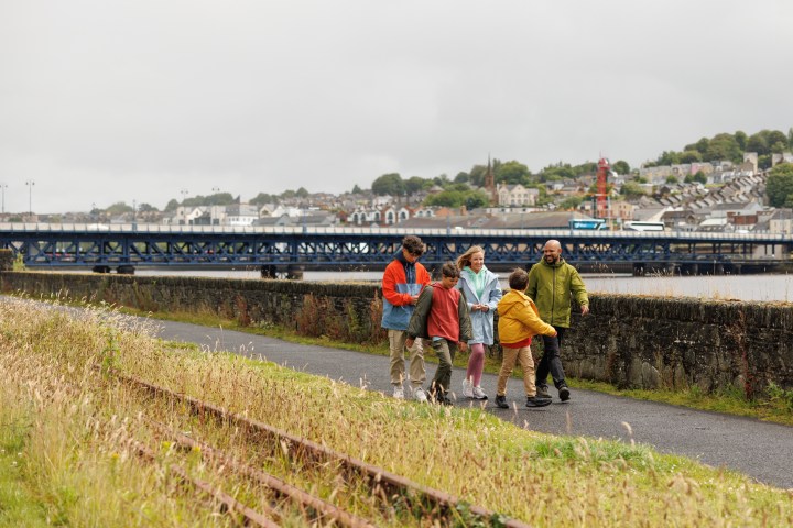 Group walking on a path near a river and bridge on a cloudy day.