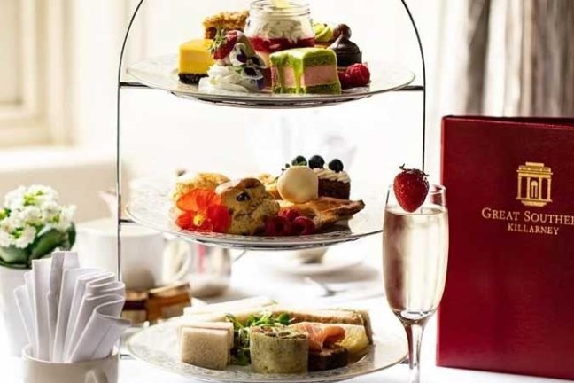 Three-tiered stand with assorted desserts, sandwiches, and a drink on a table with a red menu.