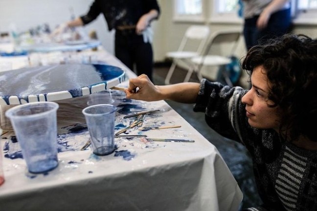 Person painting on a round canvas with blue hues in an art studio setting.