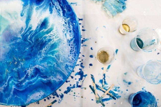 Abstract blue and white painting with cups and paint splatters on a table.