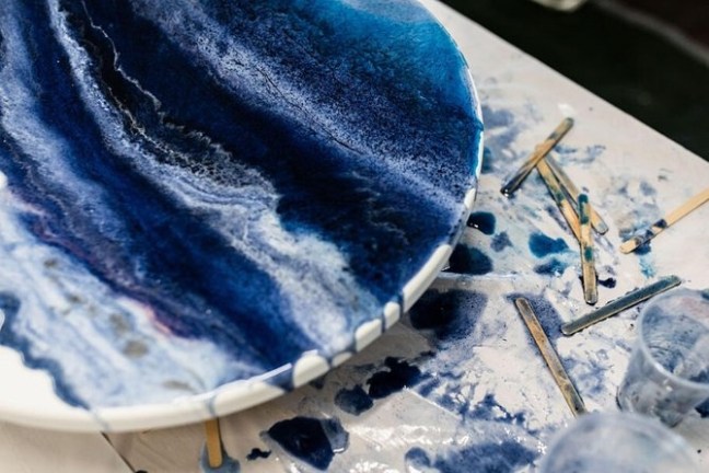 Abstract blue and white resin art on a round surface with spilled paint and sticks on a table.