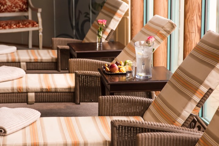Lounge chairs with striped cushions, side tables with flowers and water, and a plate of fruit indoors.