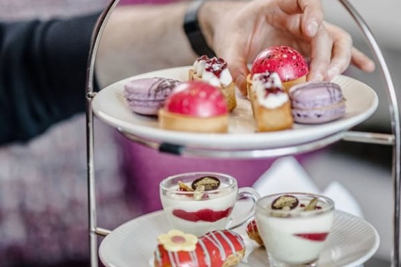 Person's hand reaching for desserts on a two-tiered platter with macarons and pastries.