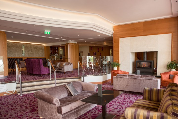 Modern hotel lounge with sofas, fireplace, and carpeted floor.
