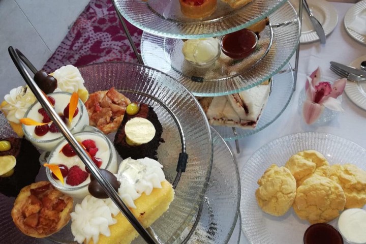 Three-tiered dessert stand with cakes, pastries, and sandwiches, next to a plate of scones and a teapot.