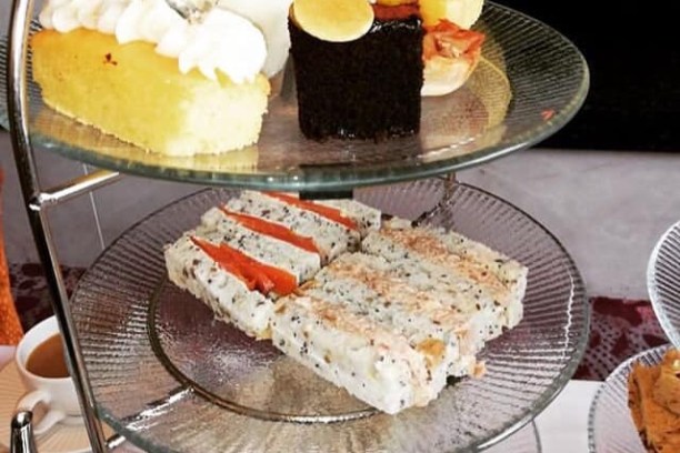 Three-tiered stand with pastries, cakes, and sandwiches, near a fireplace.