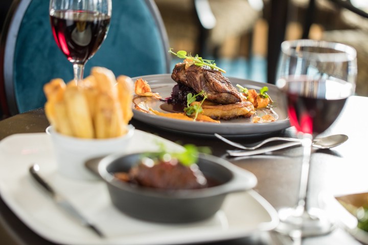 A plate with steak, fries, and glasses of red wine on a table.