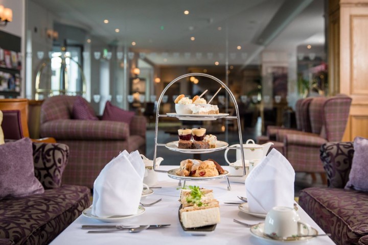 Afternoon tea setup with a three-tier stand of desserts in a cozy, elegant lounge.