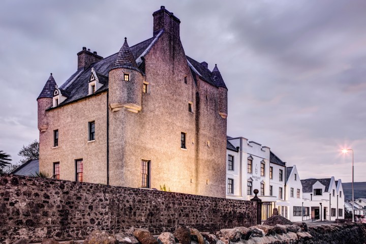 Historic stone building with turrets and modern buildings under a cloudy evening sky.