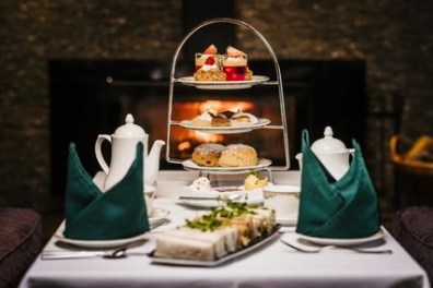 Afternoon tea with tiered tray of desserts and sandwiches in cozy setting.