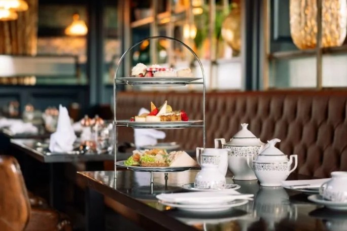 Afternoon tea setup with tiered tray and teapots on a restaurant table.