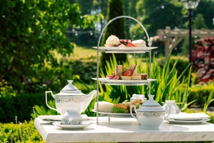 Afternoon tea set on a garden table with cakes, sandwiches, and tea pots.