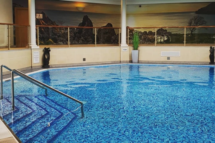 Indoor pool with mosaic tiles, steps, art mural, and large windows in a bright room.