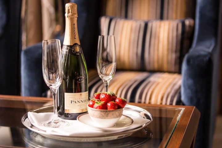 Champagne bottle with two glasses and strawberries on a tray on a table.
