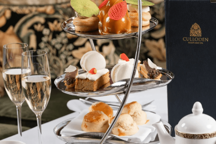 Afternoon tea set with desserts, tea, champagne, and Culloden menu on a table.