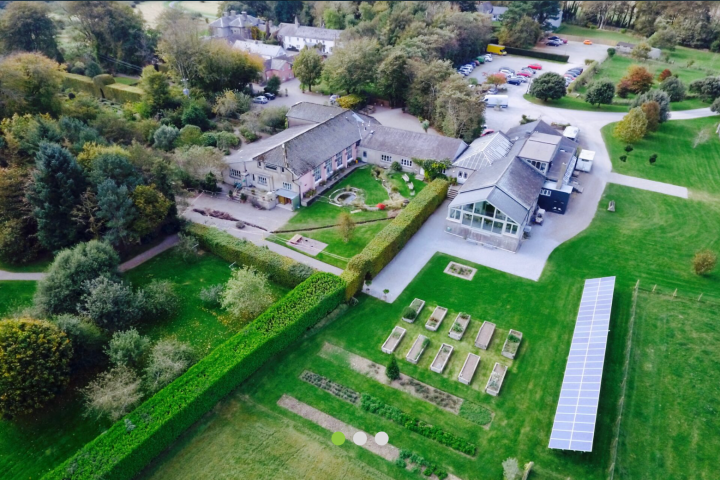 Aerial view of a large house with gardens and solar panels in a rural setting.
