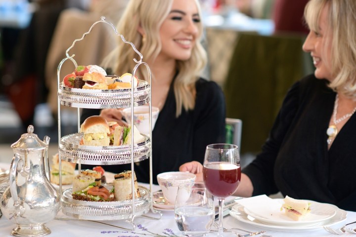 Two women enjoying afternoon tea with a tiered tray of snacks and drinks.