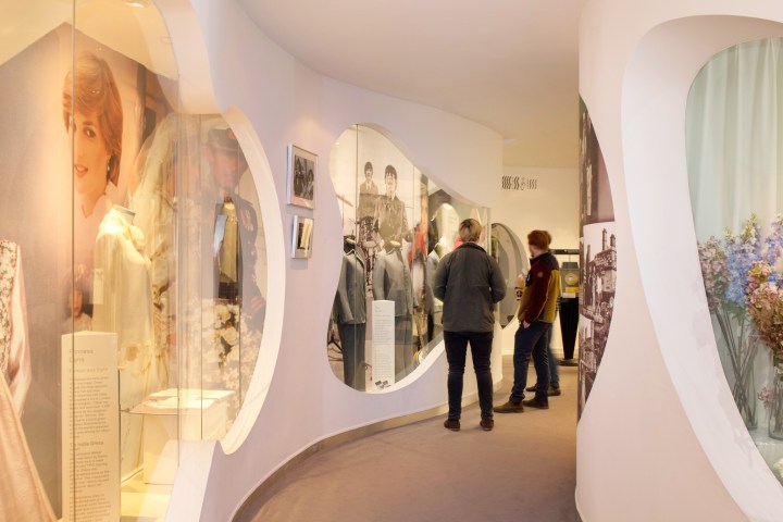 People viewing exhibits in a museum corridor with dresses and photos displayed.