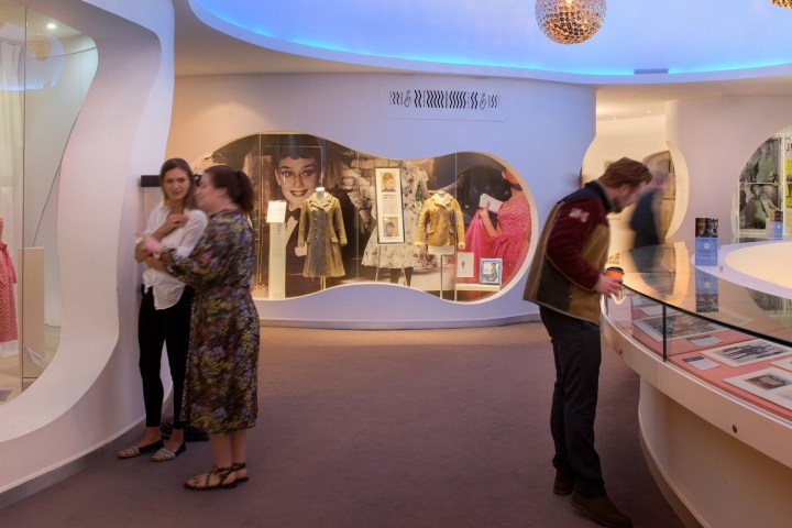 Museum exhibit with posters, vintage dresses, and visitors observing displays.