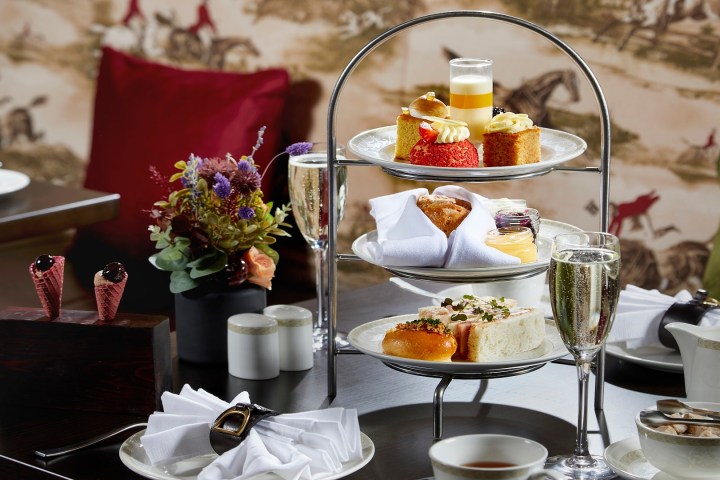 Afternoon tea setting with a three-tier cake stand, pastries, sandwiches, and a glass of champagne.
