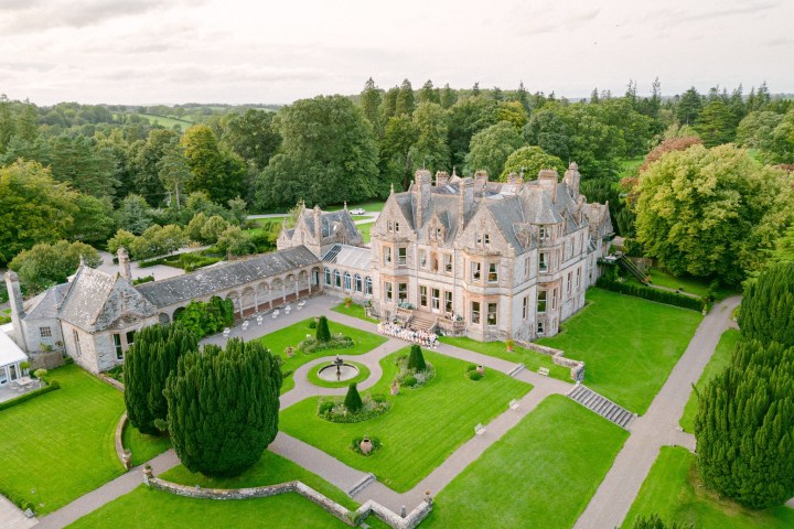 Aerial view of an elegant mansion with surrounding gardens and lush greenery.