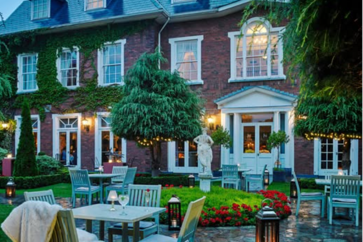 Charming ivy-covered brick house with patio tables, lanterns, and a garden statue at dusk.