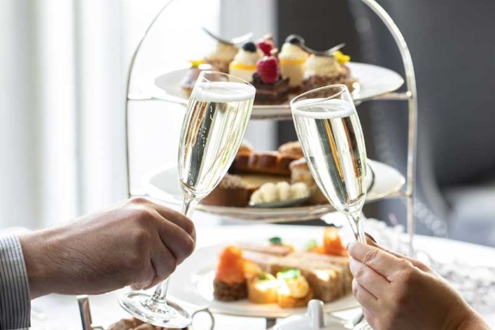 Two people clinking champagne glasses over a three-tiered platter with pastries.