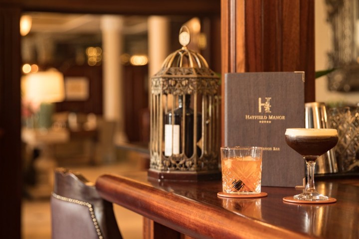 Elegant wood bar with two cocktails, menu, and decorative birdcage under chandelier.