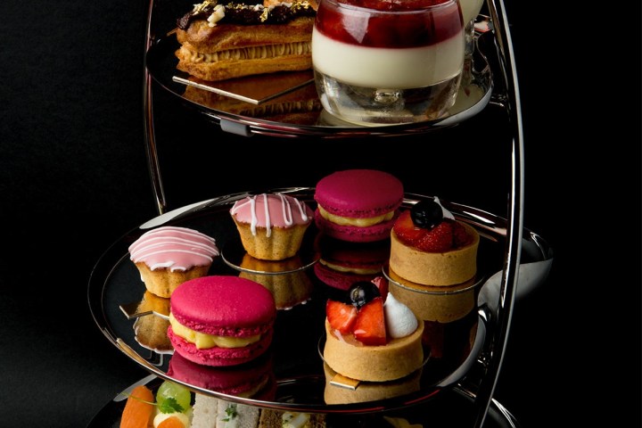 A three-tiered stand with assorted desserts and sandwiches on a black background.