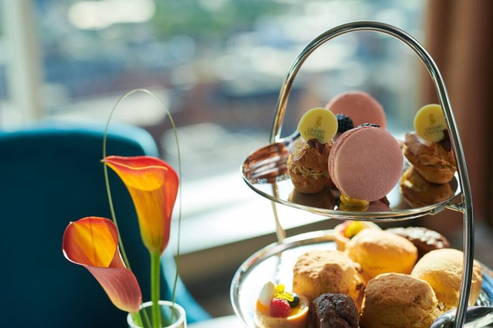 Two-tier tray with assorted pastries, macarons; vase with orange calla lilies next to it.