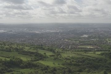 Expansive view over green hills and a distant cityscape under a cloudy sky.