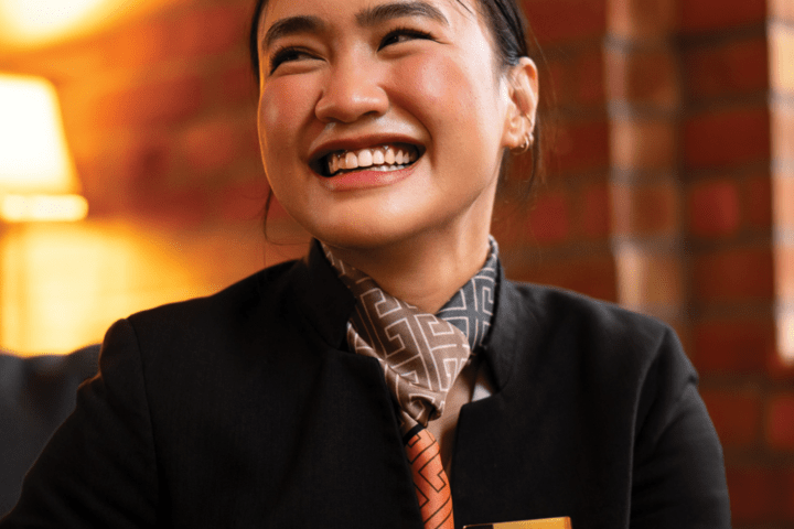 Smiling woman in uniform with nametag, indoors with warm lighting.