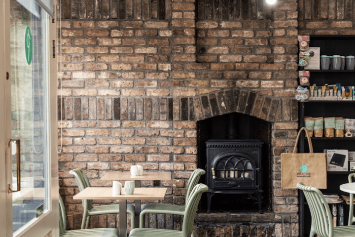 Cozy cafe with brick walls, fireplace, and small tables with chairs.