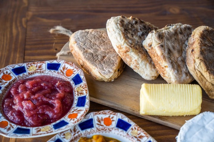 Bread, butter, fruit jam in decorative bowls on a wooden table.