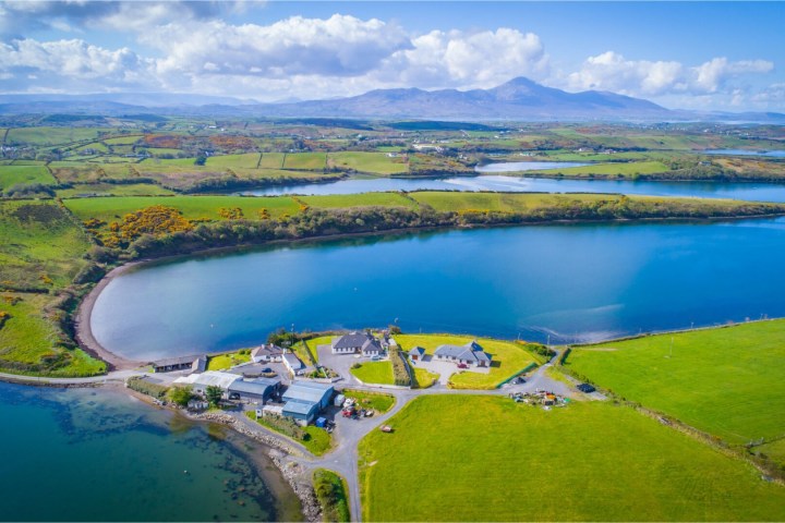 Aerial view of a coastal village with houses, green fields, and a large blue bay.