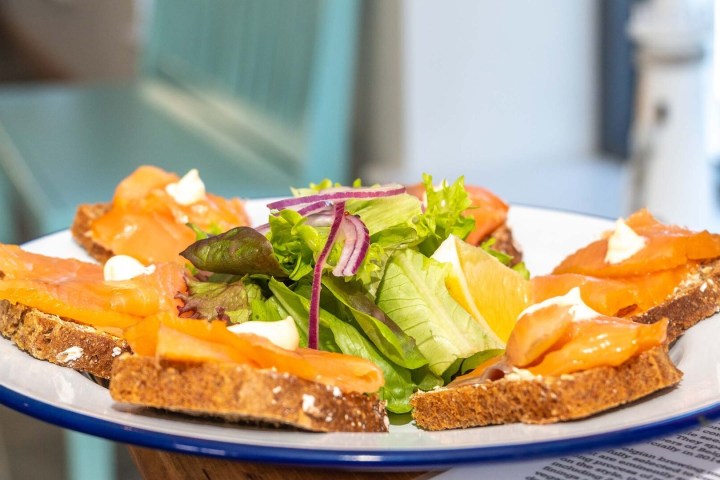 Plate of smoked salmon on bread with greens and lemon wedge in center.