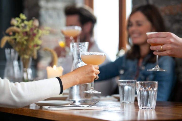 People clinking cocktail glasses at a table set with a candle and water glasses.