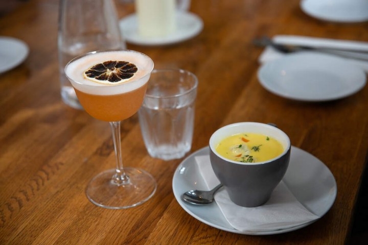 Cocktail with dried citrus, glass of water, and soup bowl on a wooden table.