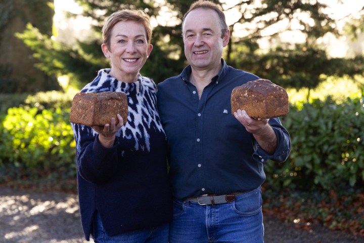 Two people smiling outdoors, each holding a loaf of bread.