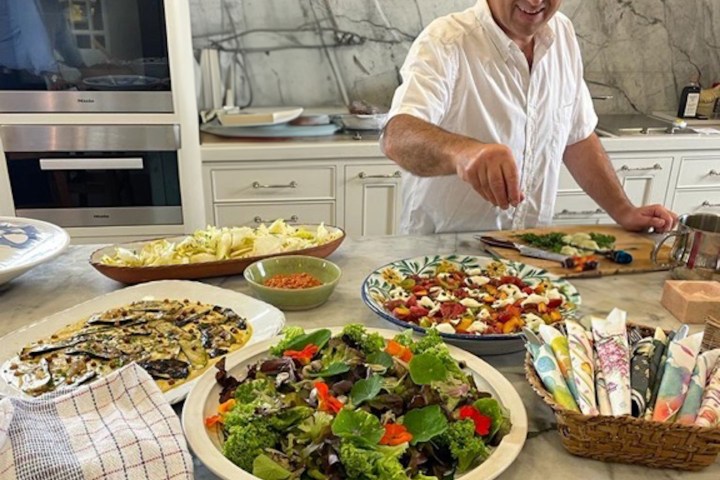 Man in white shirt preparing food in a kitchen, surrounded by dishes and a basket of napkins.